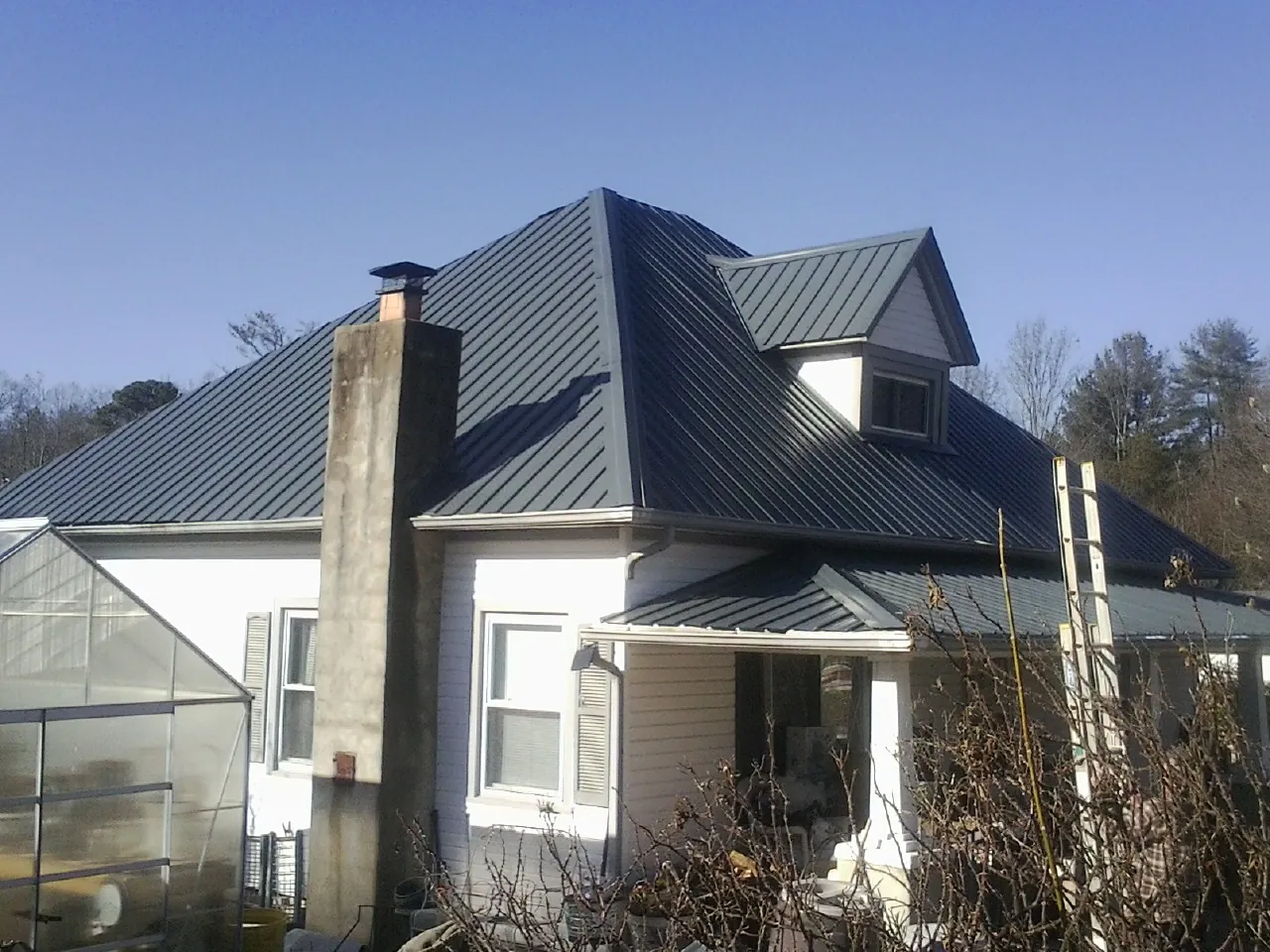 Dark blue standing seam metal roof on a white farmhouse with dormer — Slate & Tile Roof Repair by Roofing Brothers in Idaho Springs