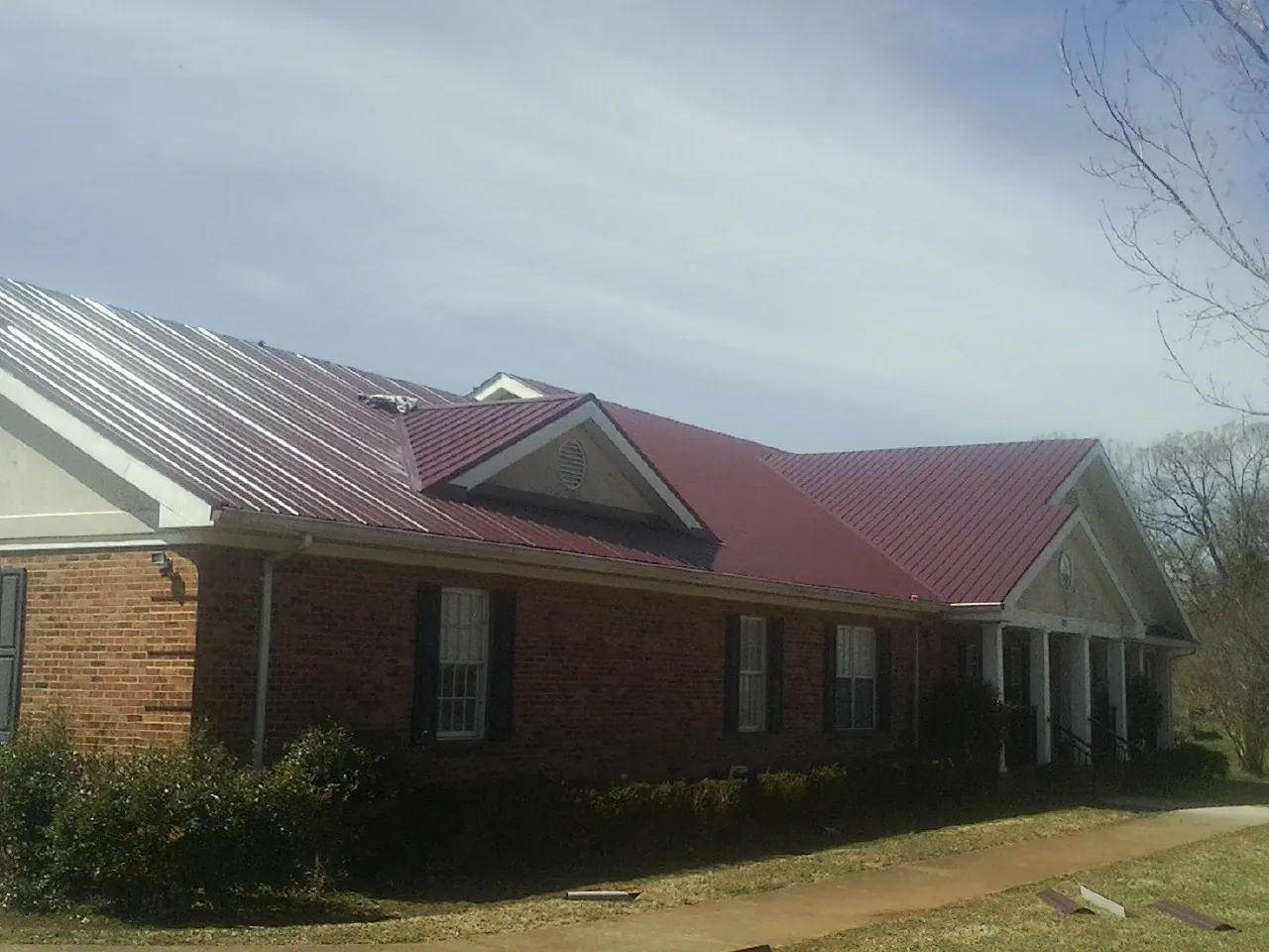 Red metal roof with gabled entries on a long brick building, from a Hail Damage Roof Repair job in Idaho Springs