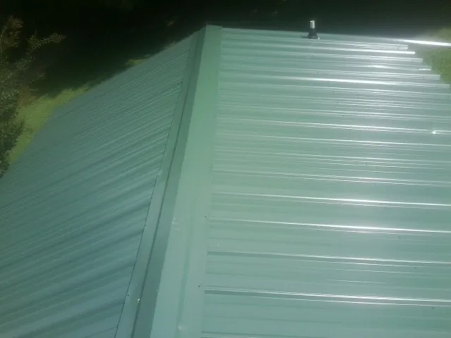 New green metal panels meeting at the ridge of a roof — Flat Roof Repair work by our crew in Idaho Springs