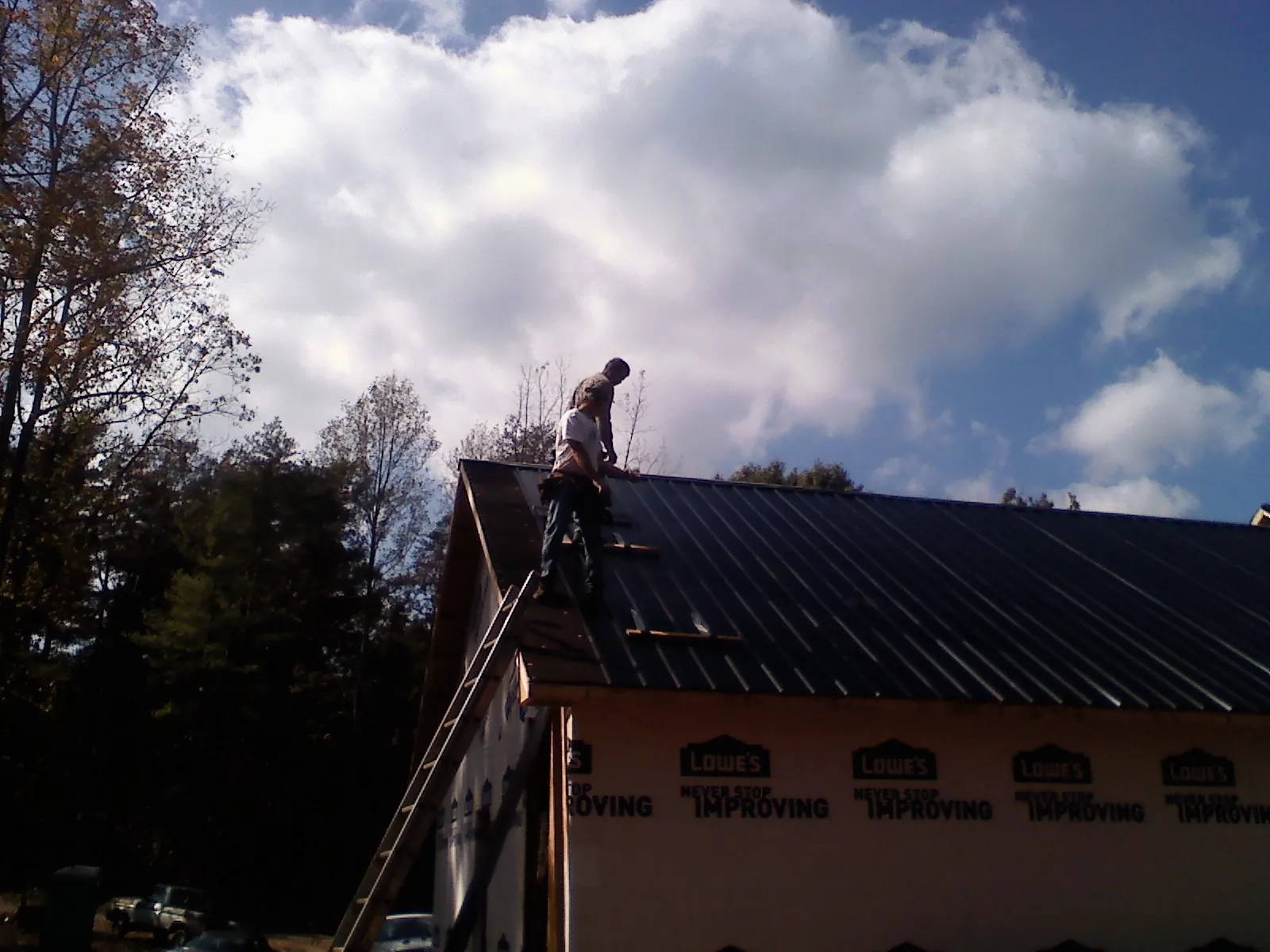Roofer fastening dark metal panels high against a cloudy sky, from a Roof Inspection job in Idaho Springs
