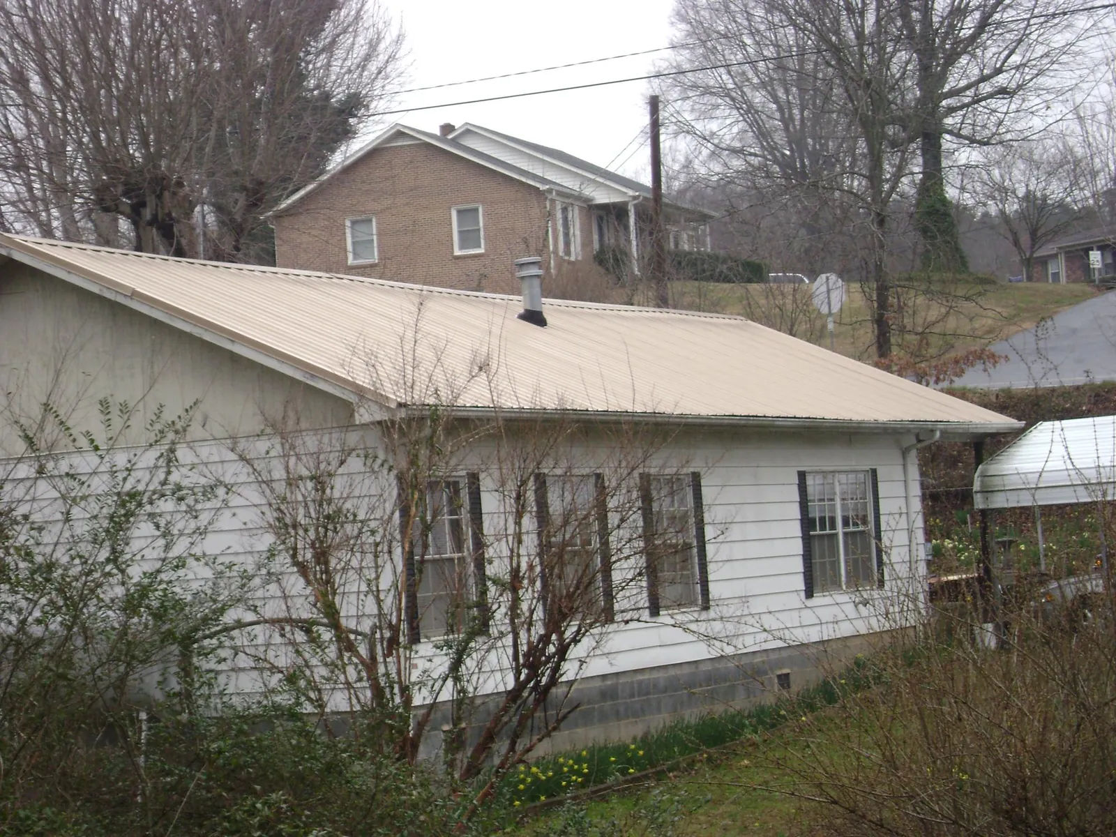 Tan metal roof on a white sided house set into a hillside — Commercial Roofing by Roofing Brothers in Idaho Springs